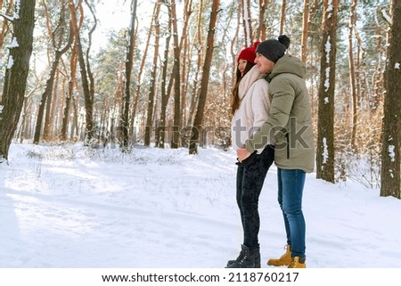 Young happy couple are standing and hugging on sunny day in snow-covered park. Men and women in a snowy winter park. Side view.