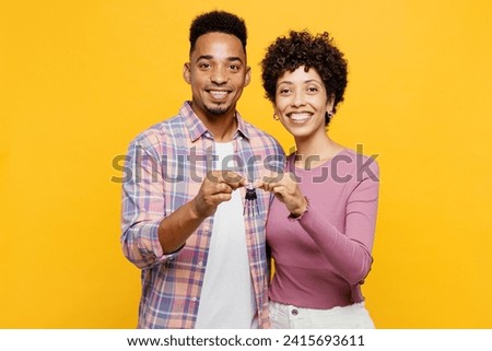 Young happy couple two friend family man woman of African American ethnicity wear purple casual clothes together hold in hand bunch of keys for new apartment isolated on plain yellow orange background
