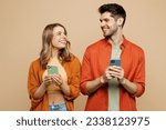 Young happy couple two friends family man woman wear casual clothes hold in hand use mobile cell phone together look to each other isolated on pastel plain light beige color background studio portrait