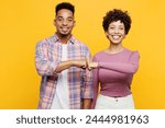 Young happy couple two friends family man woman of African American ethnicity wearing purple casual clothes together look camera do fist bump gesture isolated on plain yellow orange background studio