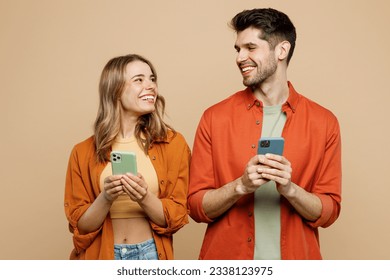 Young happy couple two friends family man woman wear casual clothes hold in hand use mobile cell phone together look to each other isolated on pastel plain light beige color background studio portrait - Powered by Shutterstock