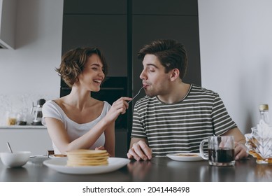 Young happy couple two woman man 20s in casual t-shirt clothes sit by table eat pancakes with maple syrup feed boyfriend cooking food in light kitchen at home together Healthy diet lifestyle concept - Shutterstock ID 2041448498