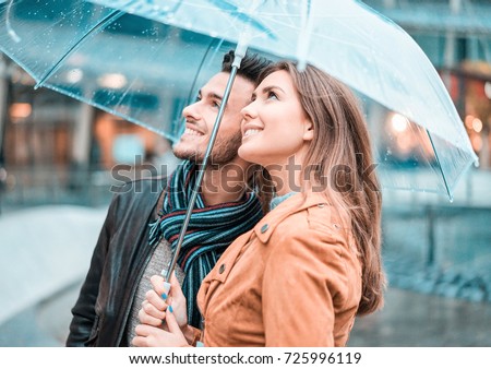 Young happy couple under the rain day covering with transparent umbrella in city center - Lovers traveling Europe during fall season - Love concept - Focus on woman face - Teal and orange filter
