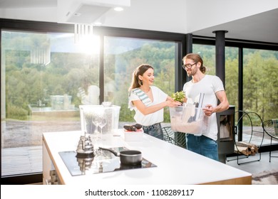 Young And Happy Couple Unpacking Different Home Stuff Making Order In Their New And Modern House