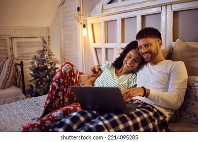 Young happy couple using laptop while relaxing on a bed at home during winter holidays.  - Powered by Shutterstock