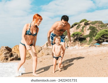 Young happy couple walking on seashore playing with running small kid and enjoying vacation on sunny day - Powered by Shutterstock