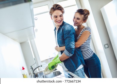 Young Happy Couple Is Washing Dishes While Doing Cleaning At Home.