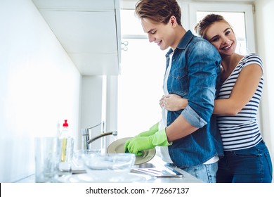 Young Happy Couple Is Washing Dishes While Doing Cleaning At Home.