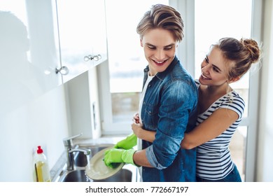 Young Happy Couple Is Washing Dishes While Doing Cleaning At Home.