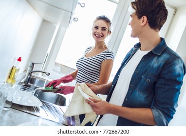 Young happy couple is washing dishes while doing cleaning at home.