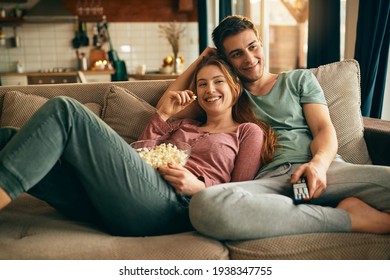 Young happy couple watching movie on TV and eating popcorn while relaxing in the living room. 