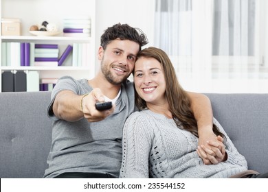 Young Happy Couple Watching TV Holding Remote Control