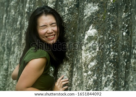 young happy and cute Asian Korean woman playing outdoors gesturing funny next to rock wall feeling carefree and having fun in youth lifestyle concept