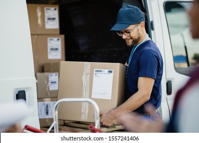 Young happy delivery man carrying cardboard box in a truck. 