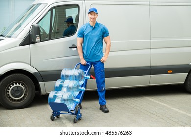 Young Happy Delivery Man Holding Trolley With Water Bottles