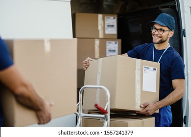 Young happy delivery man unloading boxes from a mini van and talking with his coworker. 