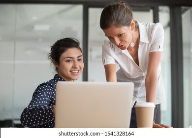 Young Happy Diverse Female Teammates Working Together On Project At Office. Senior Manager Mentor Explaining Software Program To New Employee Or Intern. Smiling Indian Worker Showing Report To Boss.