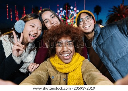 Young happy diverse group in winter clothes taking selfie portrait outdoors. Multiracial people having fun on christmas vacation. Friendship and travel concept.