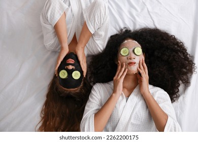 Young happy diversity ethnic beautiful woman in bathrobe lying on bed and doing cosmetic facial mask for skin care and treatment with cucumber slice. Women lesbian couple daily LGBTQ lifestyle concept - Powered by Shutterstock