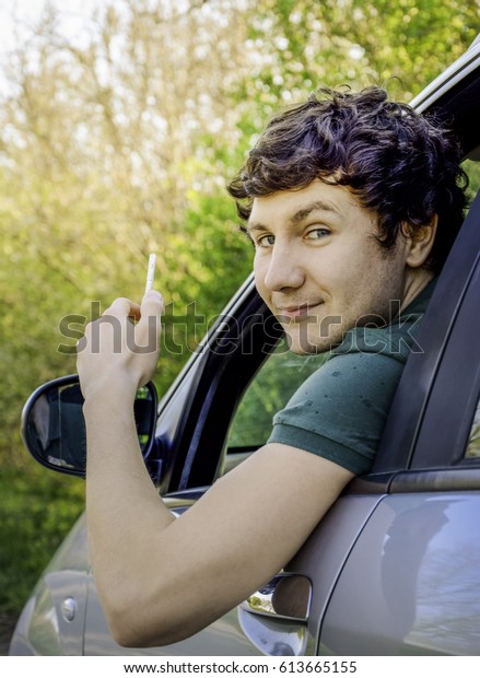 A young happy driver smiling while sitting in a\
car with open front window.