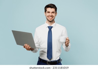 Young happy employee IT business man corporate lawyer wears classic formal shirt tie work in office hold use laptop pc computer drink coffee isolated on plain pastel blue background studio portrait - Powered by Shutterstock