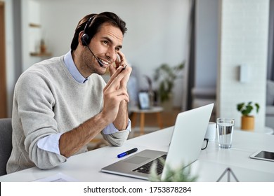 Young Happy Entrepreneur With Headset Talking With Someone While Working On A Computer At Home. 