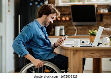 Young happy entrepreneur in wheelchair reading message on smart phone while working at home.  - Powered by Shutterstock