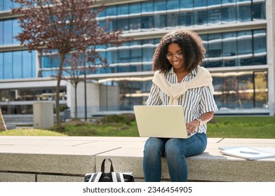 Young happy ethnic African American girl student using laptop computer learning sitting in university garden park, studying online digital remote class or elearning on pc device outdoors. - Powered by Shutterstock