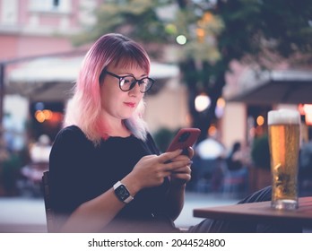 Young Happy European Woman 30 Years Old Hipster With Pink Hair With A Smartphone In Her Hands In A Street Cafe