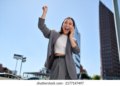 Young happy excited Asian business woman entrepreneur winner standing on city street talking on phone celebrating work success, succeed in career and financial goals raising hand in yes gesture. - Shutterstock ID 2177147497