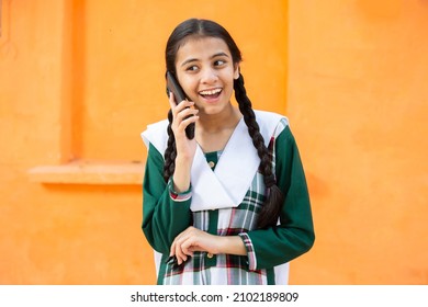 Young Happy Excited Indian Girl Talking On Smart phone against orange background, Cheerful braided female using android mobile phone or cellphone.