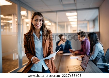 Young happy executive manager holding business meeting with her coworkers in the office and looking at camera. 