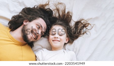Young happy family bearded father and daughter on bed in cozy home, view from top