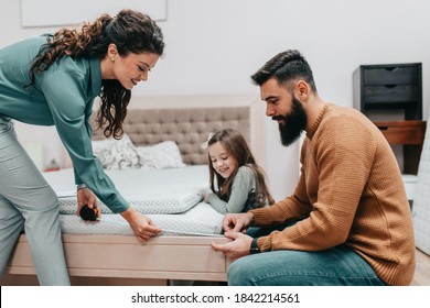 Young happy family buying new bed and mattress in big furniture store