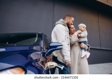 A Young, Happy Family Charges An Electric Car