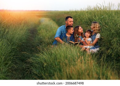 Young And Happy Family With Children Reading The Bible In Nature