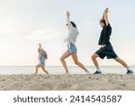 Young happy family doing yoga excercises on sunny beach. Parents and daughter meditating stretching outdoors together