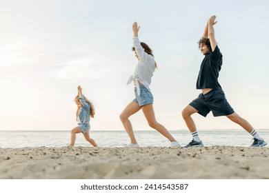 Young happy family doing yoga excercises on sunny beach. Parents and daughter meditating stretching outdoors together - Powered by Shutterstock