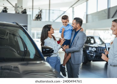 Young happy family enjoying while buying a new car in a showroom. Saleswoman at car dealership center helping family to choose new family vehicle. Family in a car dealership  - Powered by Shutterstock