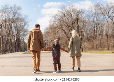 Young Happy Family Father Mother And Son. View From Behind. Walking By City Park