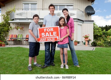 Young Happy Family Holding Sold Sign Outside Their New House