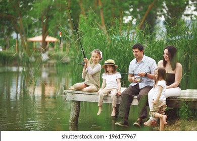 Young Happy Family With Kids Fishing In Pond In Summer