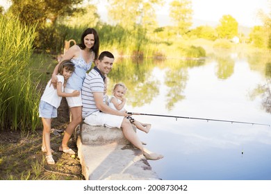 Young Happy Family With Kids Fishing In Pond In Summer