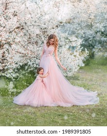 Young Happy Family, Mom And Daughter In Beautiful Evening Festive Long Powdery Pink Color Dresses. Little Girl Hugs Woman, Looks With Love Smile On Face. Fashiom Model Matching Same Clothes Outfit Set