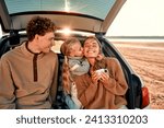 A young happy family on a picnic with their beloved little daughter sitting in the back of a car on a blanket on a weekend having fun together.