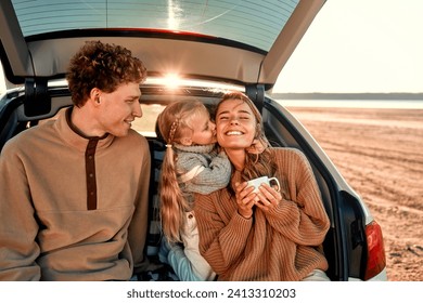 A young happy family on a picnic with their beloved little daughter sitting in the back of a car on a blanket on a weekend having fun together. - Powered by Shutterstock