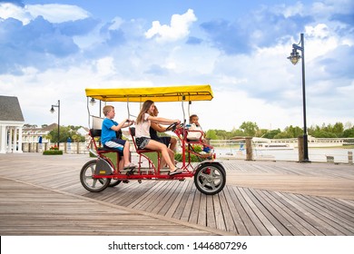 Young happy family riding a double surrey tandem bicycle on a large ocean boardwalk. Outdoor summer fun with kids
