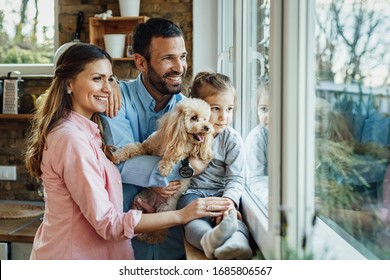 Young Happy Family And Their Dg Relaxing By The Window At Home And Looking Through It. 