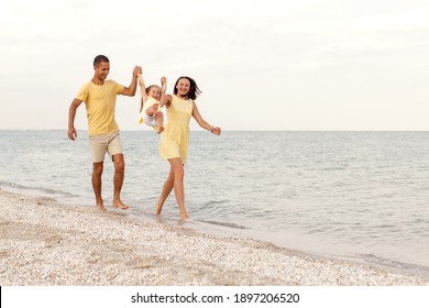 Young happy family in yellow walks by the sea. Parents play with their child in the fresh air.