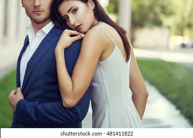 Young Happy Fashionable Couple In The City In Stylish Sunglasses.The Man Wearing In Business Suit, The Woman In Romantic Sexy Dress With Lace.